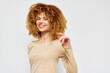 © SHOTPRIME STUDIO - Smiling woman with curly hair in a beige sweater against a light background, exuding positivity and confidence, perfect for lifestyle and beauty themes