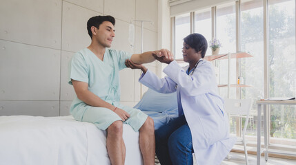 Wall Mural - Patient caucasian man with woman nurse carer physical therapist black people two person sitting talk helping support give advice and holding hand arm inside clinic hospital indoor room service.