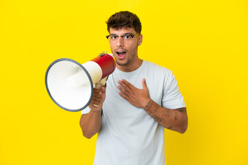 Sticker - Young caucasian handsome man isolated on yellow background shouting through a megaphone with surprised expression