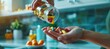 © spyrakot - A woman's hand pours colorful vitamin capsules from a transparent bottle into her palm, set against a modern kitchen background. highlights a focus on health, wellness