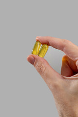 Showcasing vitamins, dietary supplements, and nutrition products. Woman holding two omega-3 capsules in her hand.  Intake of healthy fats, omega-3 fish oil. Medicine advertising mockup