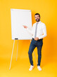 © luismolinero - Full-length shot of businessman giving a presentation on white board over isolated yellow background pointing finger to the side