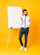 © luismolinero - Full-length shot of businessman giving a presentation on white board over isolated yellow background making money gesture