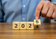 © Hanna - Man flipping a block from 4 to 5 while showing the year 2025 on a wooden table