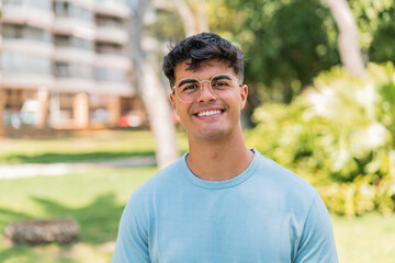 Wall Mural - Young hispanic man at outdoors With glasses with happy expression