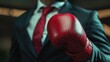 © Cherkasova Alie - A businessman wearing a suit holds red boxing gloves, showcasing a bold contrast against a blurred urban background.
