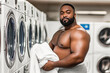 © Elena - Muscular black man holding clean laundry at laundromat, feeling confident and strong