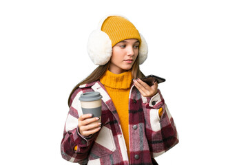 Sticker - Teenager caucasian girl wearing winter muffs over isolated background holding coffee to take away and a mobile