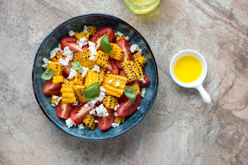 Wall Mural - Blue bowl with tomato and grilled corn salad, flat lay on a brown granite background, horizontal shot