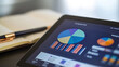 © atipong - A pie chart and bar graph on a tablet, accompanied by a sleek pen and notebook in the background, symbolizing financial planning.