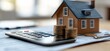 © VINA - A calculator, a toy house, and coins representing homeownership expenses.