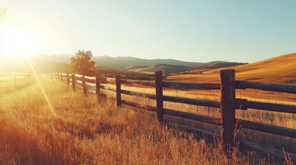 Poster - Rustic wooden fence under the warm glow of sunset with distant rolling hills and golden fields