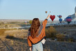 © VICHIZH - Woman excitedly points at colorful hot air balloons floating in the sky above a vast green field
