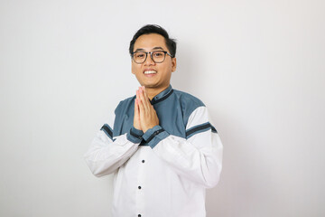 Portrait of attractive Asian muslim man in koko shirt with skullcap showing apologize and welcome hand gesture. Apology during eid mubarak. Isolated image on white background