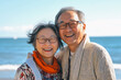 © 1005mm photography - An elderly Chinese couple smiling in glasses against the backdrop of a seaside landscape.