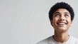 © Thanapol - A young boy with curly hair smiles brightly while looking upwards, conveying joy and positivity in a minimalistic setting