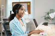 © amnaj - Friendly female support employee managing helpline service, typing on keyboard and talking with customer online using hands free device