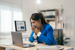 © Parichat - Young businesswoman with a surprised expression is sitting at her desk, covering her mouth with her hands while looking at her laptop, reacting to unexpected news or data