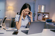 © Parichat - Young office worker suffering from a migraine, touching her temples while sitting at her desk with laptop and paperwork, feeling tired and overworked