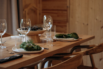 Christmas table setting featuring a fir branches, a cones, a green napkins against the background of a wooden table.