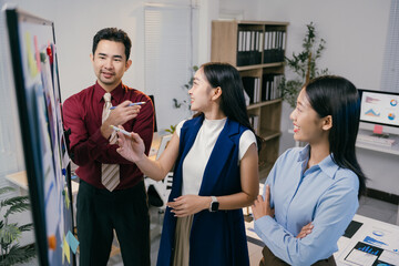 Wall Mural - Group of young asian businesspeople analyzing charts and graphs on whiteboard, sharing ideas and discussing strategy during a productive meeting in a modern office