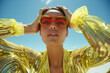 © Femmes.Digital - Model in vibrant yellow sequined dress with red oversized sunglasses, posing under a bright sunny sky. Bold fashion editorial with a strong summer vibe and glamorous flair.