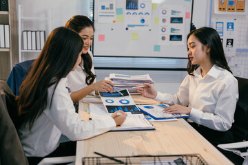 Fototapete - Three asian businesswomen are sitting at a desk reviewing financial charts and discussing business strategy in a modern office