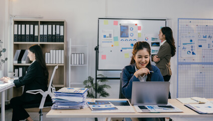 Wall Mural - Asian businesswomen are analyzing financial charts on laptop computer and whiteboard, collaborating and brainstorming for successful business strategy in modern office meeting room