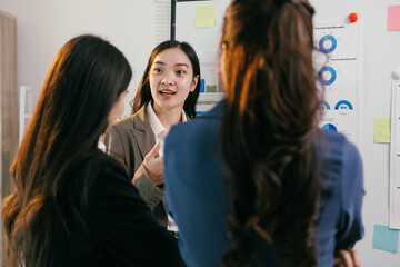 Fototapete - Three asian businesswomen are having a discussion about marketing strategy in a modern office, standing in front of a whiteboard with charts and graphs