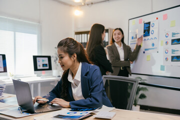Fototapete - Businesswomen are collaborating on a project, analyzing charts and reports on a laptop and whiteboard, demonstrating teamwork and data-driven decision-making in a modern office environment