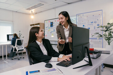 Wall Mural - Two cheerful businesswomen are working together on a computer, discussing strategies and analyzing data in a bright, modern office environment, fostering teamwork and collaboration