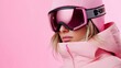 © milenialdesastudio - A woman in a pink ski jacket and goggles with a pink beanie on against a pink background.