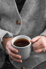 Wall Mural - Woman in grey cozy sweater holding mug with espresso coffee close up.