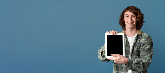 Smiling teenage guy showing tablet computer with empty screen on turquoise background, space for design