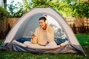 young woman listening to music or audio book in tent in backyard