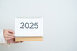 © Jo Panuwat D - Business woman hand holding and change 2025 Year Calendar on white background table in office. countdown, Happy New Year, Resolution, Year End and New Start and Goals Plan Action Concept