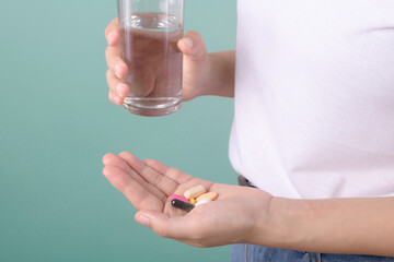 closeup woman hand holding medicine overdose pills and glass of water isolated on green background.