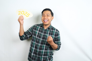 excited asian man showing victory and winning gesture while holding 2025 board isolated on white background