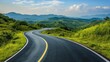 © B 7 YOU - A winding asphalt road curves through a lush green mountain landscape under a bright blue sky with fluffy white clouds.