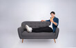 © STOCK88PHOTOGRAPHER - Full body image of young Asian man using phone sitting on sofa on white background