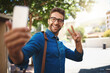 © peopleimages.com - Happy man, travel and selfie with peace sign in city for photography, picture or social media. Young, handsome or male person with smile or emoji for memory, capture or outdoor moment in neighborhood