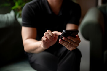 A close-up of a man using his smartphone on a sofa indoors.