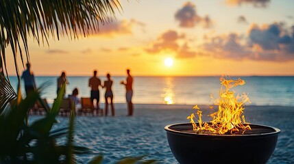 Sunset beach scene with a fire pit and silhouettes of people enjoying the view.