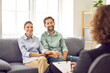 © Studio Romantic - Cheerful family couple meeting with professional therapist or psychologist. Happy husband and wife having therapy session, sitting on couch, holding hands, talking about their relationship and smiling