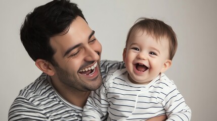 A father holds his baby boy and they both laugh.