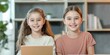 © Kamonwan - Two smiling girls pose with a laptop in a cozy indoor setting.