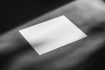 Aufkleber - A single sheet of blank white paper resting at an angle on a textured dark surface, highlighted by light and shadow, creating a minimalist and contemplative scene.