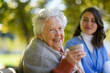 © Halfpoint - Elderly woman enjoying cup of coffee with her nurse in the park during warm autumn day. Young caregiver spending time with senior woman.