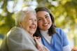 © Halfpoint - Portrait of nurse and elderly woman on walk in the park during warm autumn day. Young caregiver spending time with senior patient.