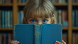 © Cristina - little girl child reads a blue book and looks out from behind it, eyes and a smile are visible, school tomorrow.